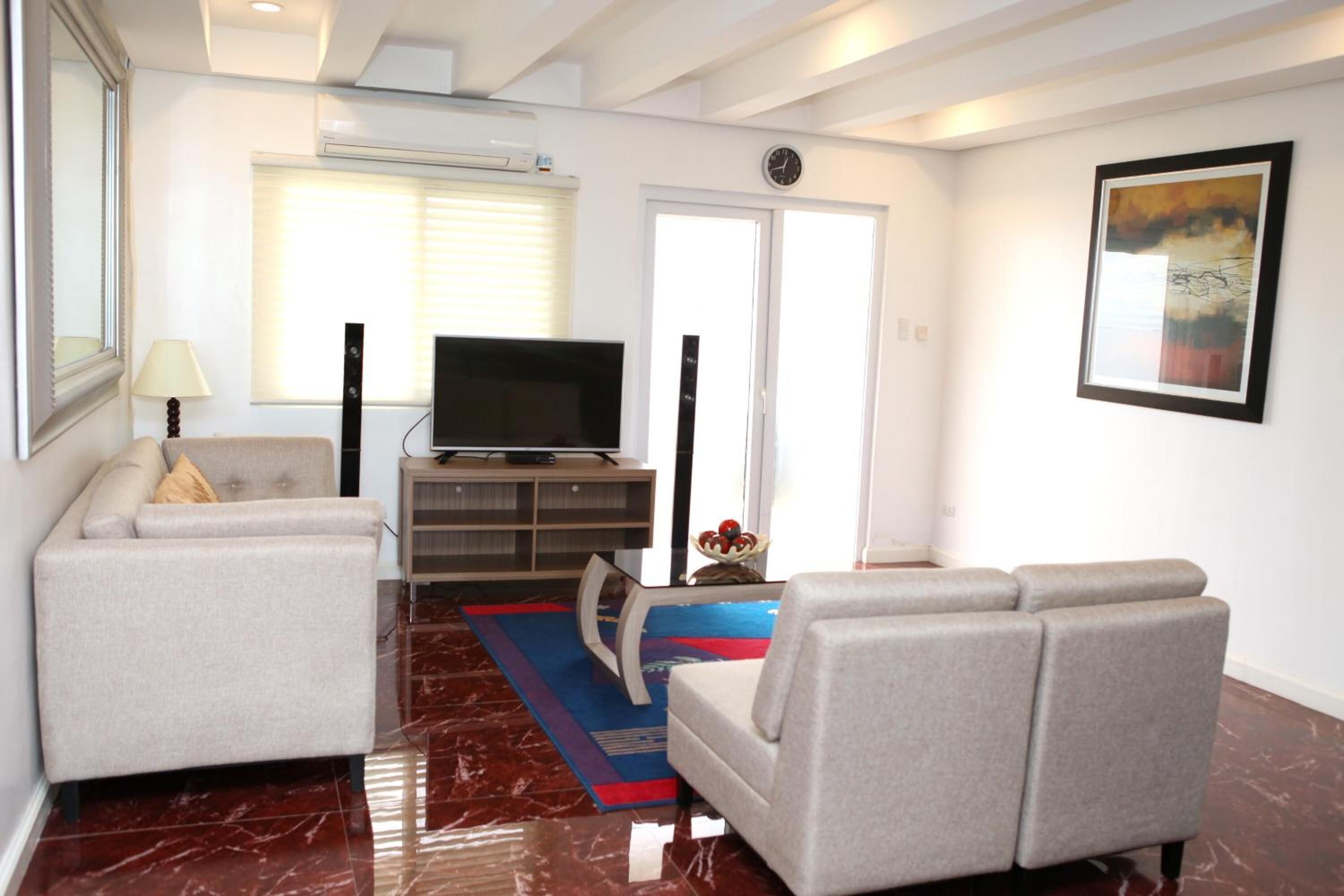 A modern living room with a sofa, a television on a stand, and a red and blue rug.