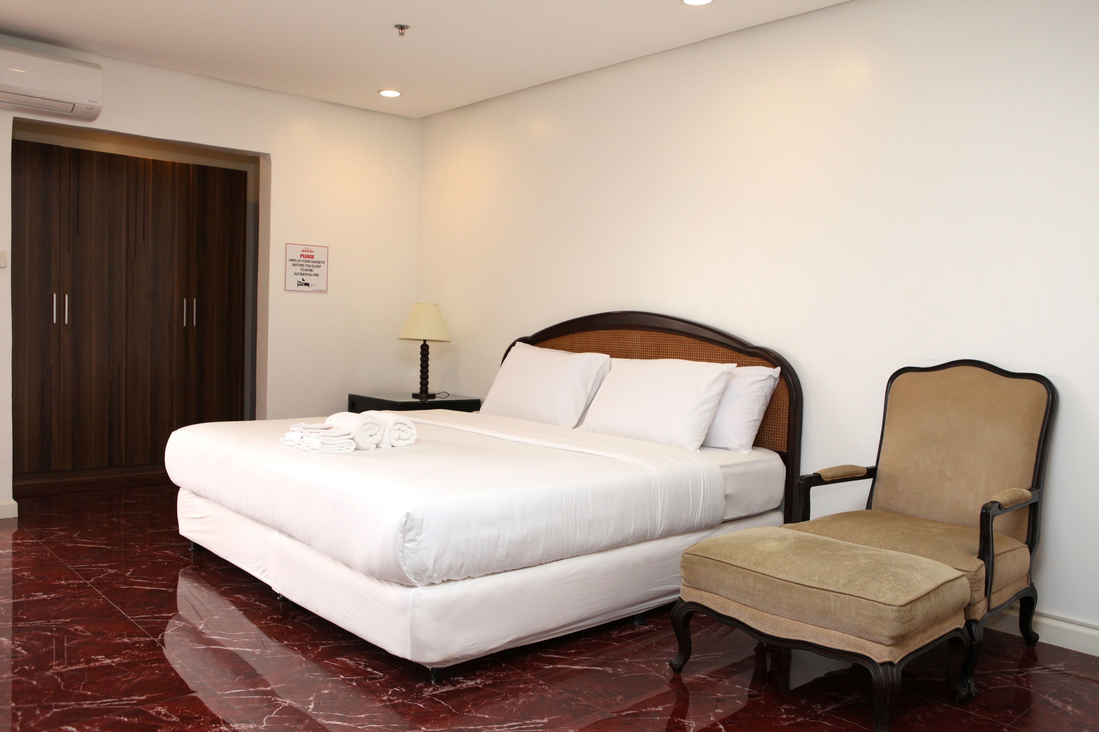 A neatly made bed with white linens, a wooden headboard, and a matching armchair.
