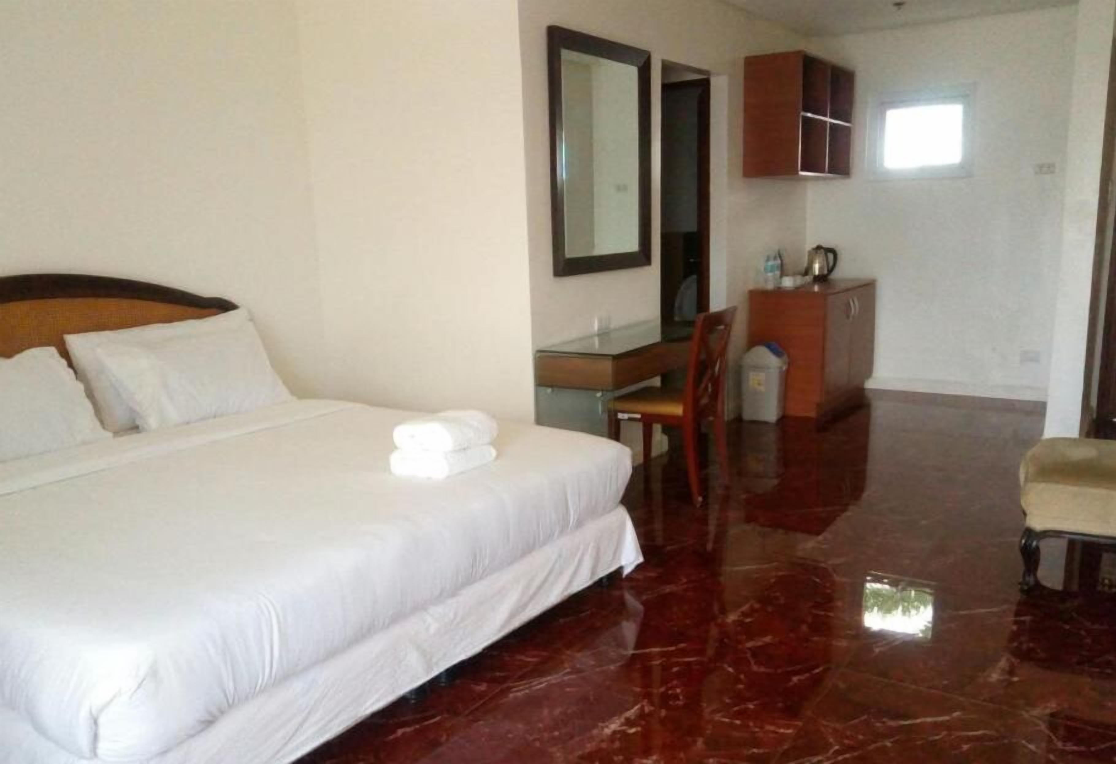 A hotel room with a large bed, a desk, a chair, a wardrobe, and a small window.