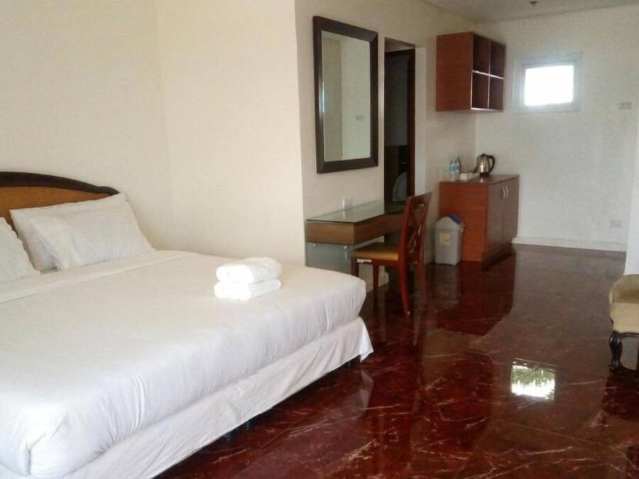 A hotel room with a large bed, a desk, a chair, a wardrobe, and a small window.