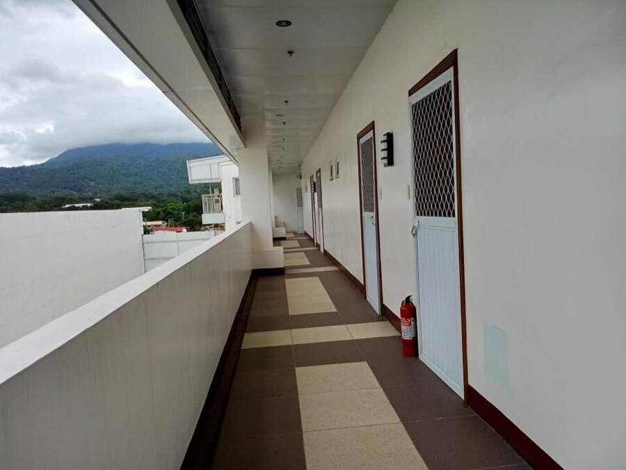 A corridor with a tiled floor, white walls, and doors with metal grilles.