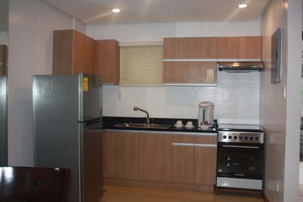 Cocina compacta con alacenas de madera, refrigerador de acero inoxidable, pileta y horno empotrado.
