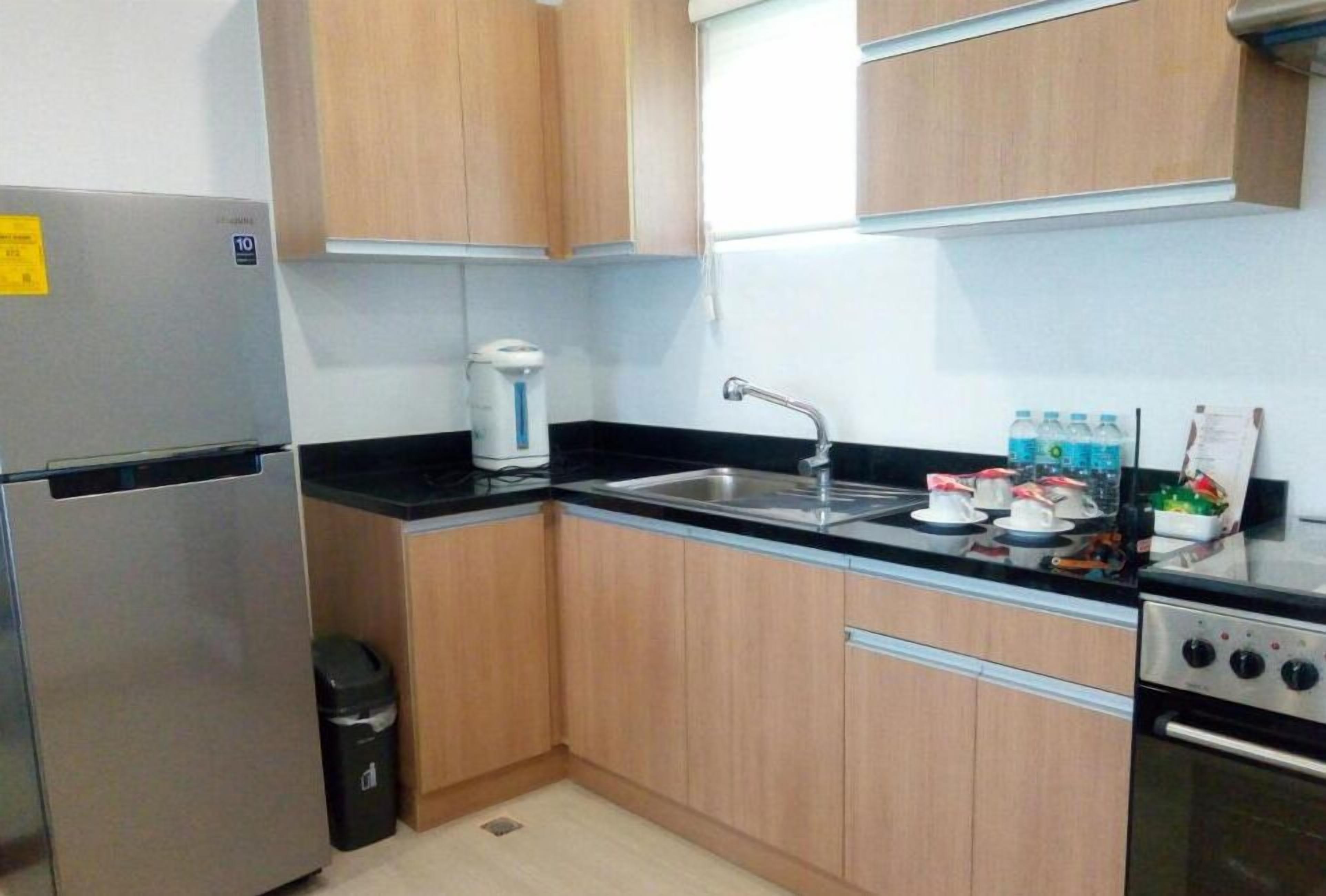 A compact kitchen with wooden cabinets, a stainless steel refrigerator, a coffee maker, a sink, and a stove.