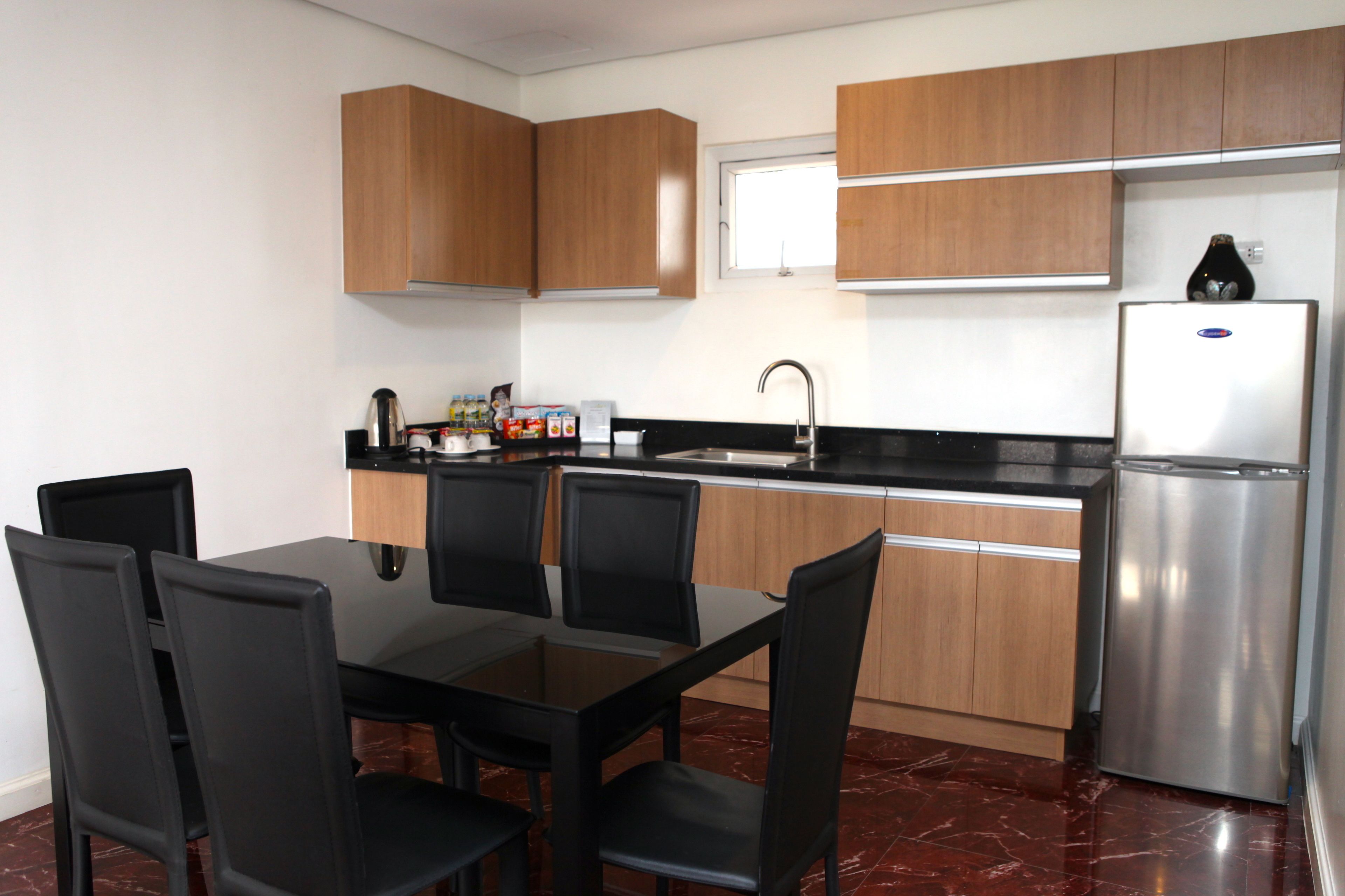 A modern kitchen with wooden cabinets, a stainless steel refrigerator, a black countertop, and a dining table with chairs.