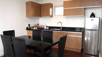 A modern kitchen with wooden cabinets, a stainless steel refrigerator, a black countertop, and a dining table with chairs.