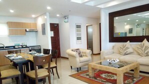 A modern living room with a sofa, coffee table, and dining area with chairs and a table. - Centtro Residences (Los Banos)