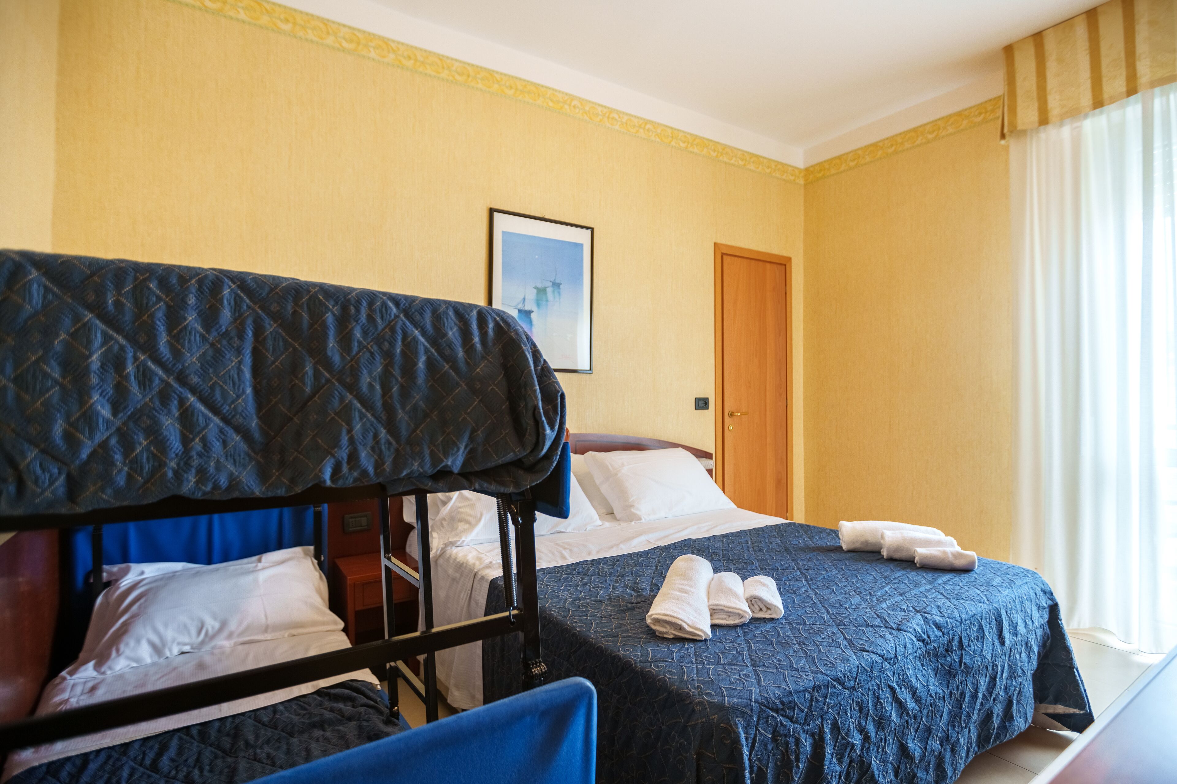 A hotel room with two beds, a wooden headboard, a framed picture on the wall, and a window with curtains.