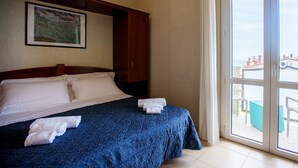 Une chambre d’hôtel avec un lit, un tableau au mur et une vue sur l’extérieur, visible à travers une porte vitrée.