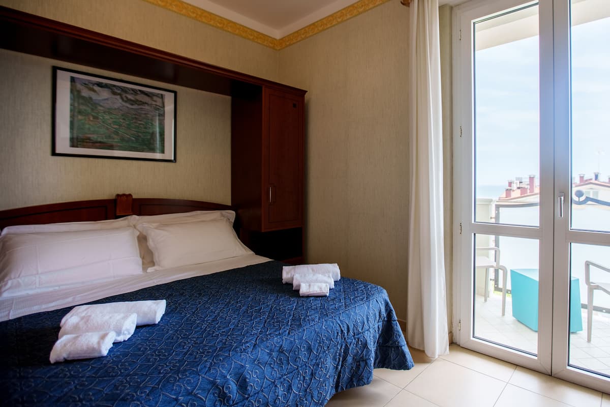Habitación de hotel con cama, un cuadro en la pared y vistas al exterior a través de un ventanal.