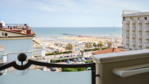 Une vue sur une plage, prise depuis un balcon, avec un ciel dégagé, un parking et un immeuble doté de balcons.