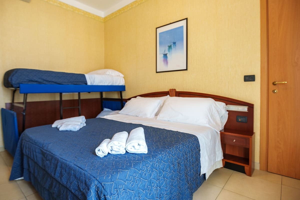 Una habitación de hotel con una cama individual, una cama litera, una mesita de noche de madera y una puerta.
