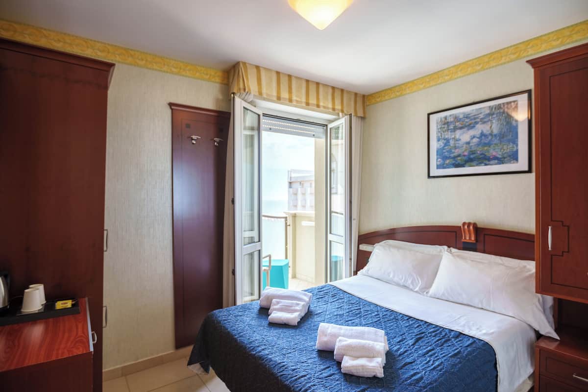 Habitación de hotel con cama, armario, puerta que da a un balcón y un cuadro en la pared.