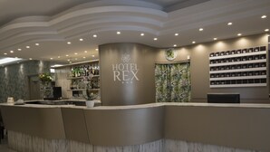 Un espace d’accueil d’hôtel avec un comptoir en marbre, une horloge et un mur où sont exposés divers objets.