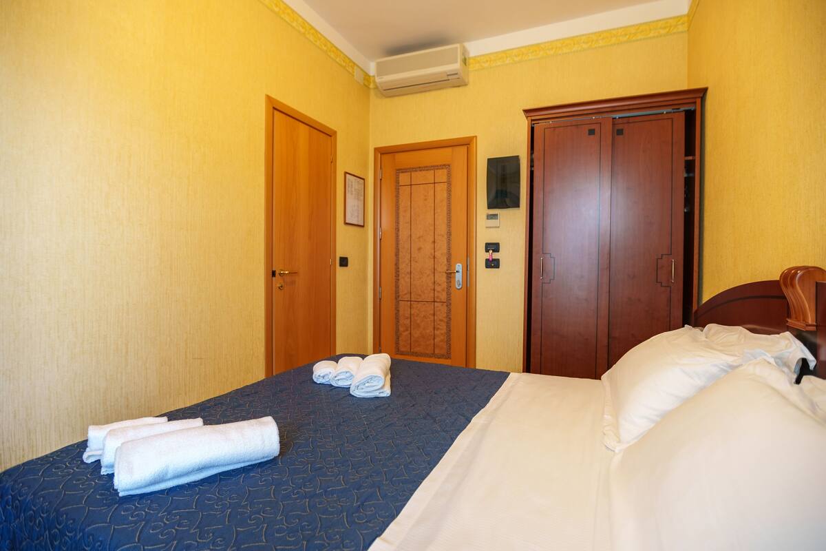 Una habitación de hotel con una cama, dos puertas y un aire acondicionado instalado en la pared.