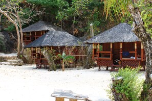 A thatched-roof bungalow with a wooden deck and a stone bench. - Bamboo Private Islands (Culion Island)
