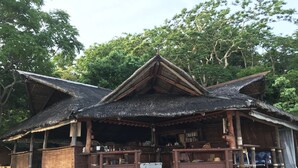 A traditional wooden house with a thatched roof, wooden benches, and a small porch area. - Bamboo Private Islands (Culion Island)