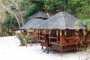 Thatched-roof huts with wooden railings and benches, situated on a sandy area with sparse vegetation. - Bamboo Private Islands (Culion Island)