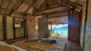 A room with a bed, a window with a view of the sea, and a thatched roof. - Bamboo Private Islands (Culion Island)