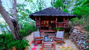 A thatched-roof hut with a wooden interior, surrounded by a colorful rug and seating area. - Bamboo Private Islands (Culion Island)