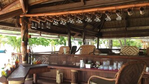 A bar area with wicker furniture, a wooden counter, and hanging wine glasses. - Bamboo Private Islands (Culion Island)