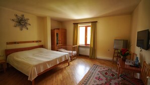 A bedroom with a wooden bed, a small table with a vase of flowers, a chair, a wooden cabinet, and a window with curtains.