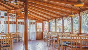 A spacious dining area with wooden tables and chairs, large windows, and a tiled floor. - Hotel Mirhav (Goris)