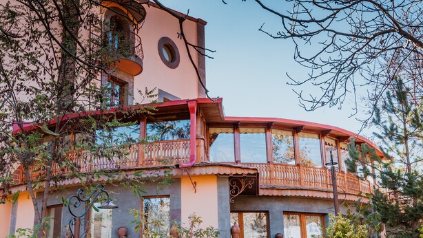 A multi-story building with balconies, large windows, and a stone base. - Hotel Mirhav (Goris)