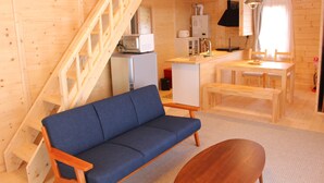 Ein Holzblockhaus-Interieur mit einer Couch, einem Holzesstisch, einer Küchenzeile und einer Treppe.