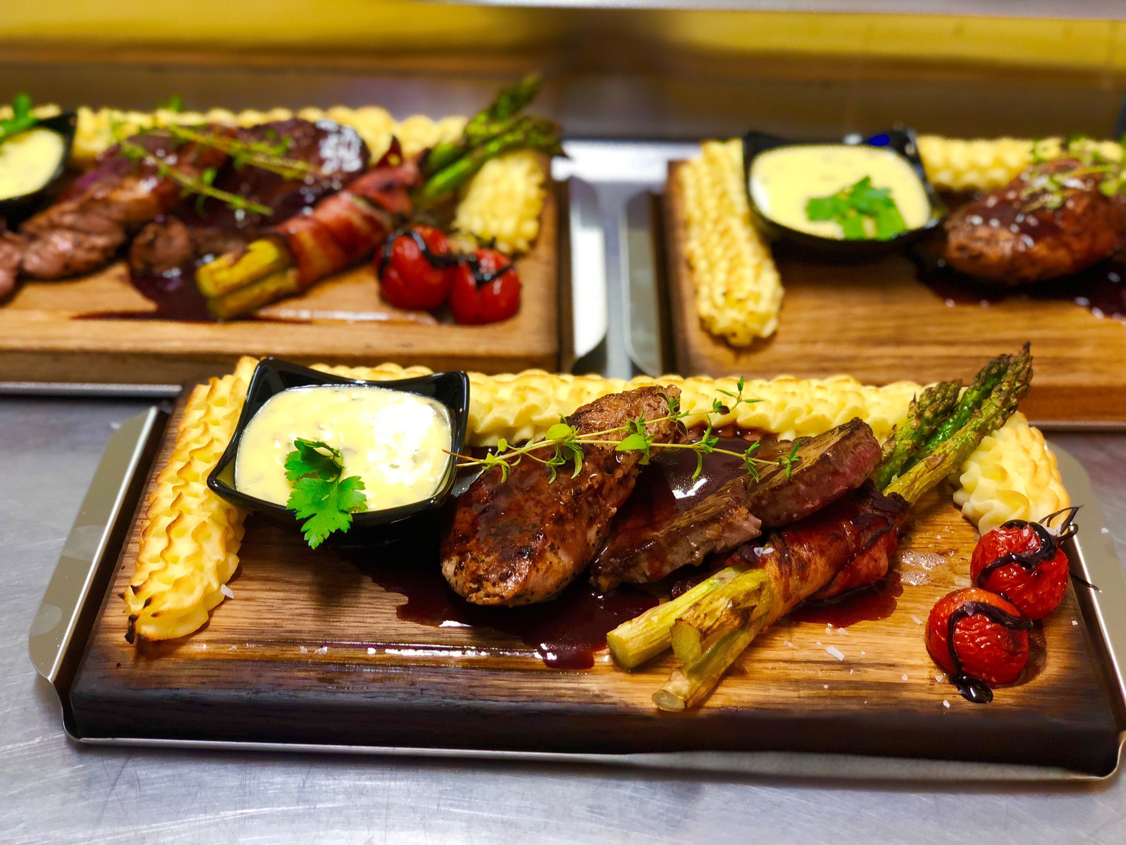 Un piatto con carne alla griglia, asparagi e pomodorini, servito con purè di patate e una piccola ciotola di salsa.