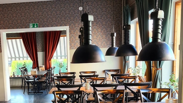 Een restaurant met houten tafels en stoelen, zwarte hanglampen en behang met een patroon.