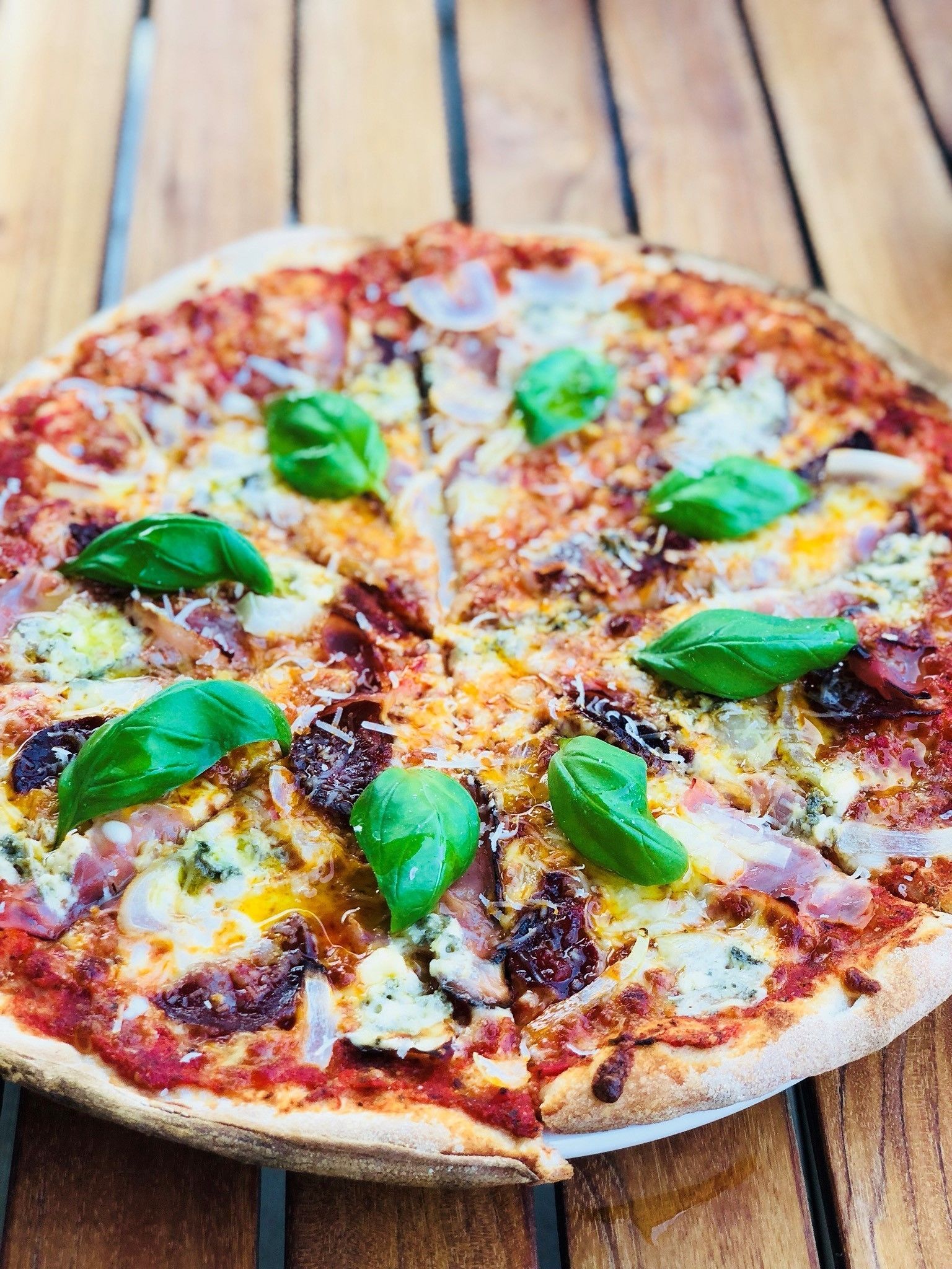 A pizza with various toppings and basil leaves on a wooden table.