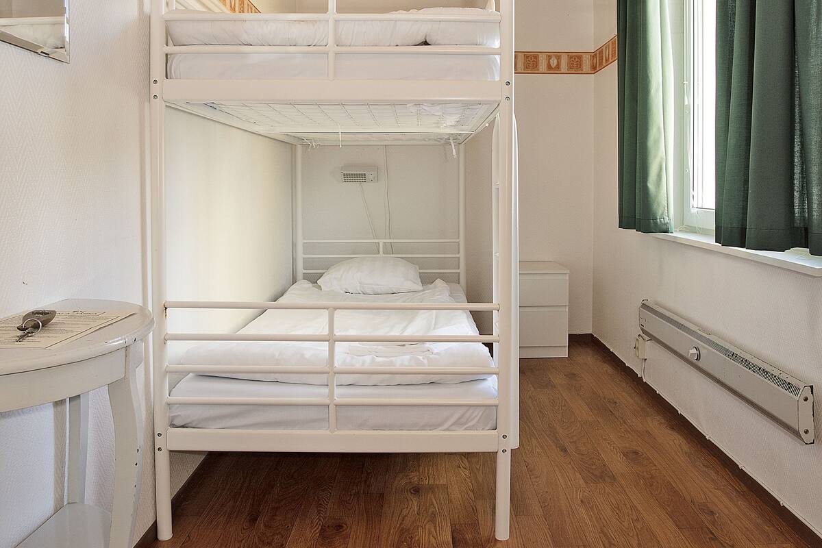 Une chambre avec un lit superposé, un plafond en bois, une petite table et une fenêtre avec des rideaux.