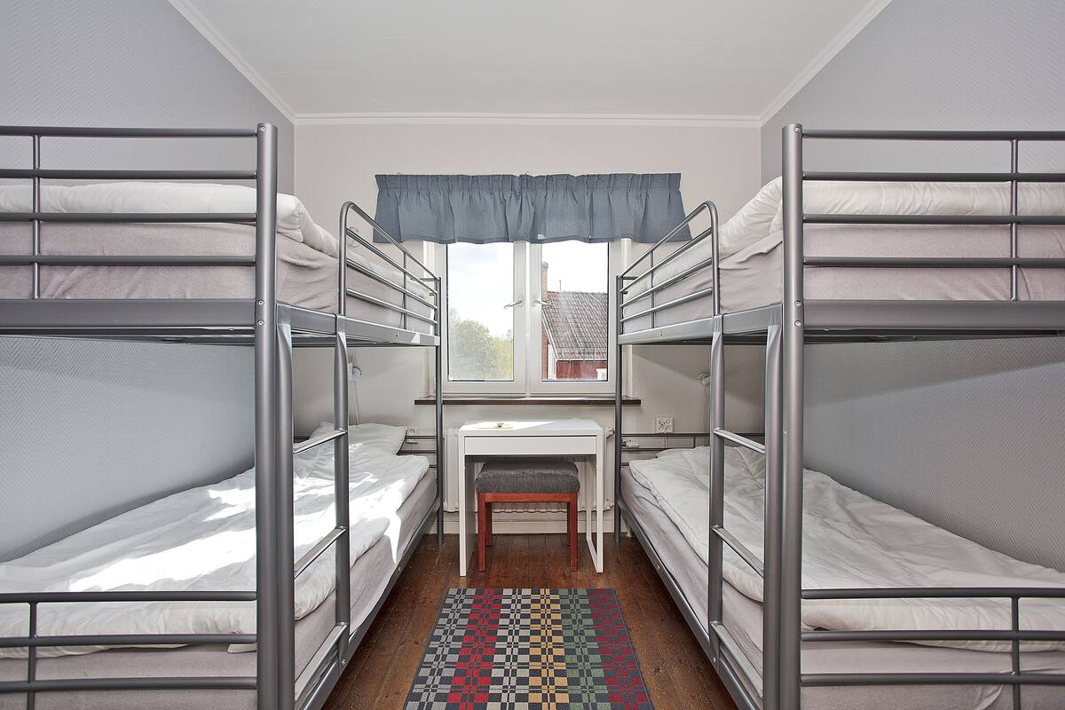 Une chambre de dortoir avec des lits superposés, un petit bureau et une fenêtre donnant sur un bâtiment à l’extérieur.