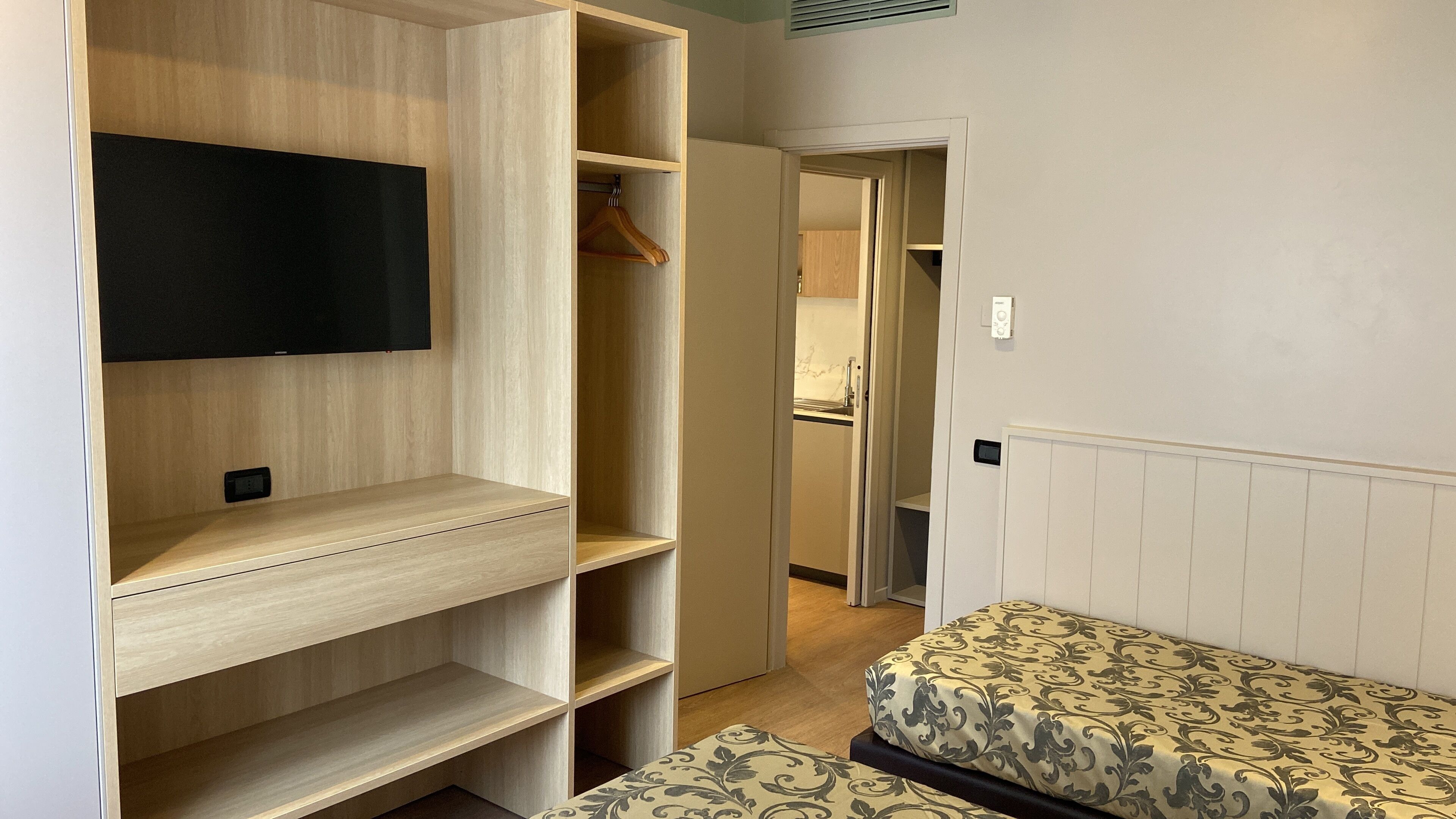 Une chambre d’hôtel dotée d’une grande armoire, d’un lit avec une literie à motifs et d’un téléviseur fixé au mur.