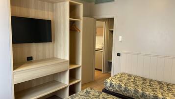 A hotel room with a large wardrobe, a bed with patterned bedding, and a television mounted on the wall.