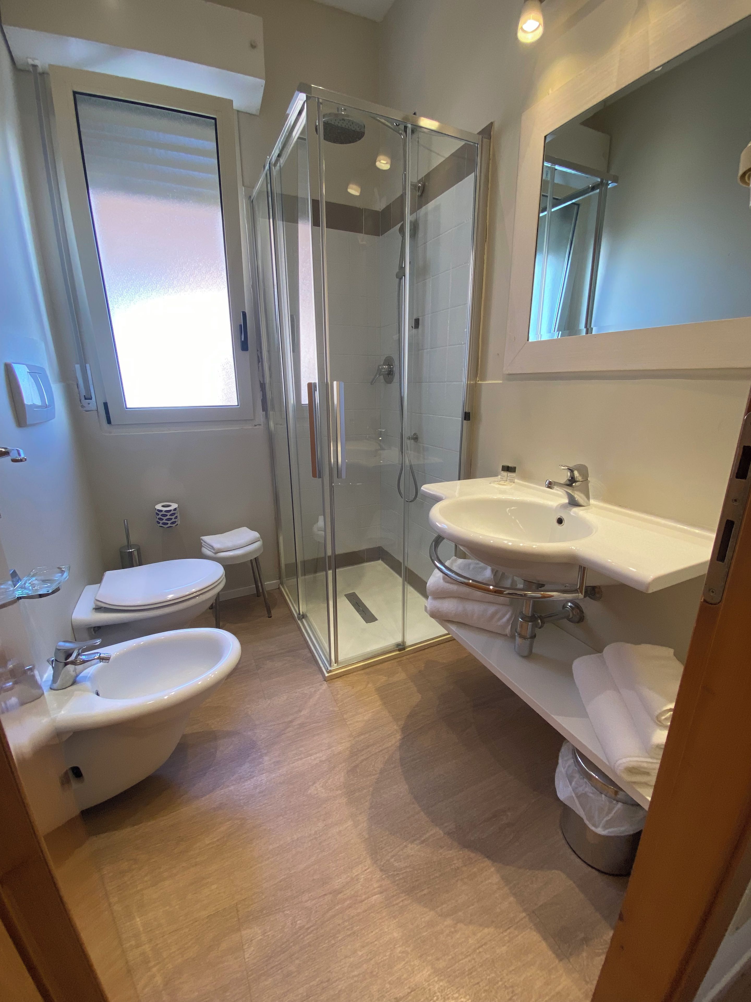 A modern bathroom with a glass-enclosed shower, two sinks, a toilet, and a large mirror.
