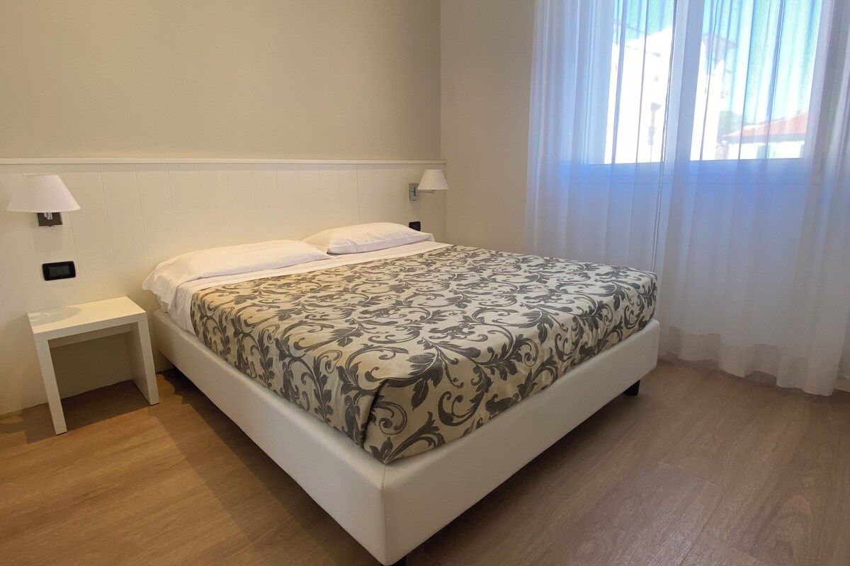 Una habitación de hotel con cama, mesitas de noche y una ventana con cortinas.