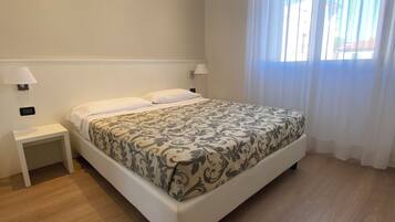 Une chambre d’hôtel avec un lit, des tables de chevet et une fenêtre avec des rideaux.