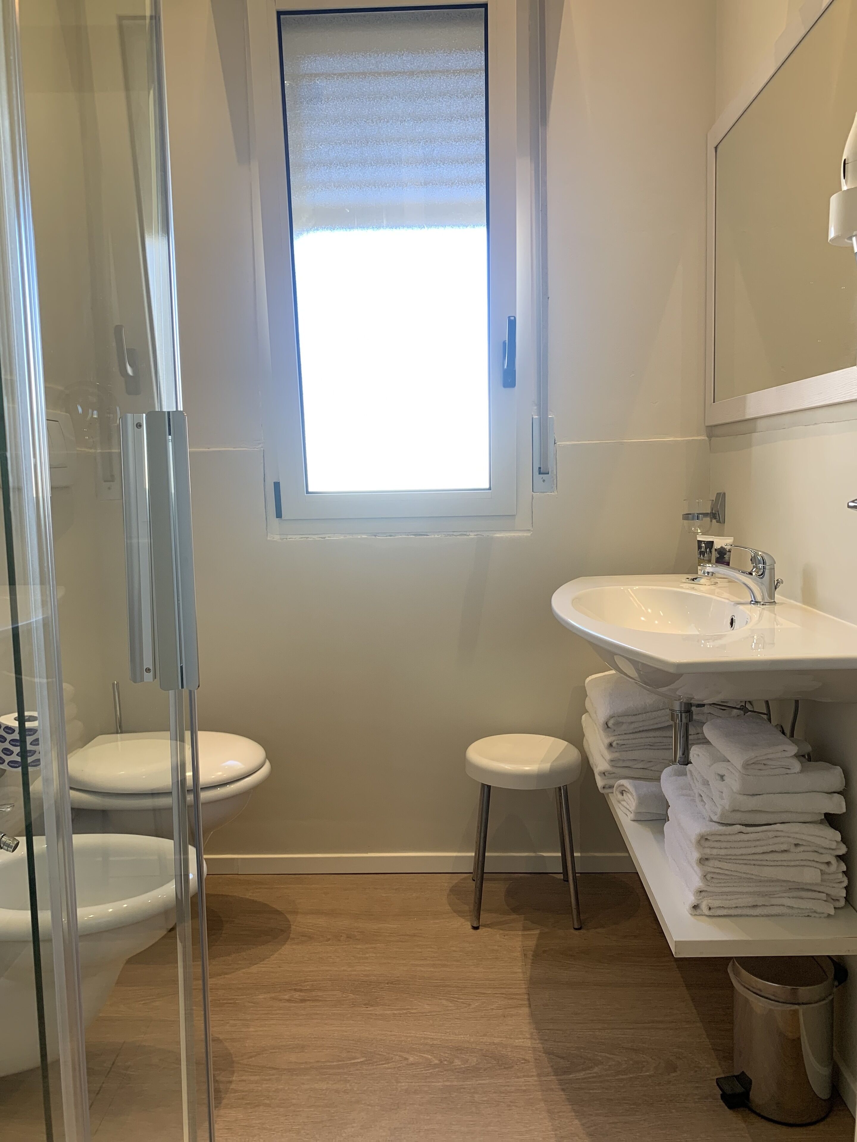 A bathroom with a toilet, a sink, a mirror, a window, and a glass shower enclosure.