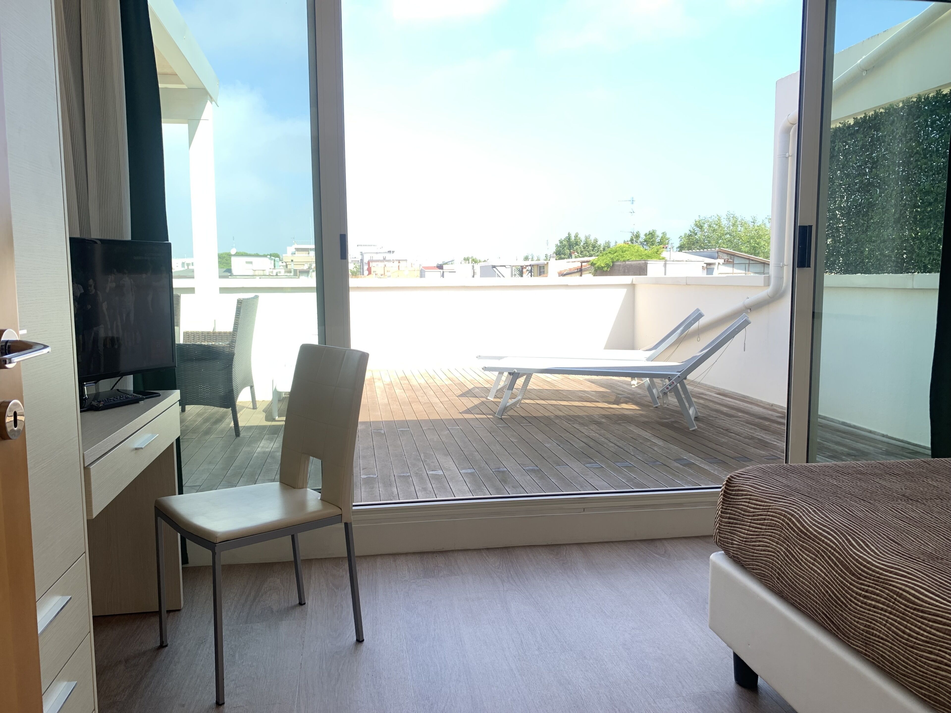 A hotel room with a balcony, a TV, a chair, a bed, and a view of the cityscape.