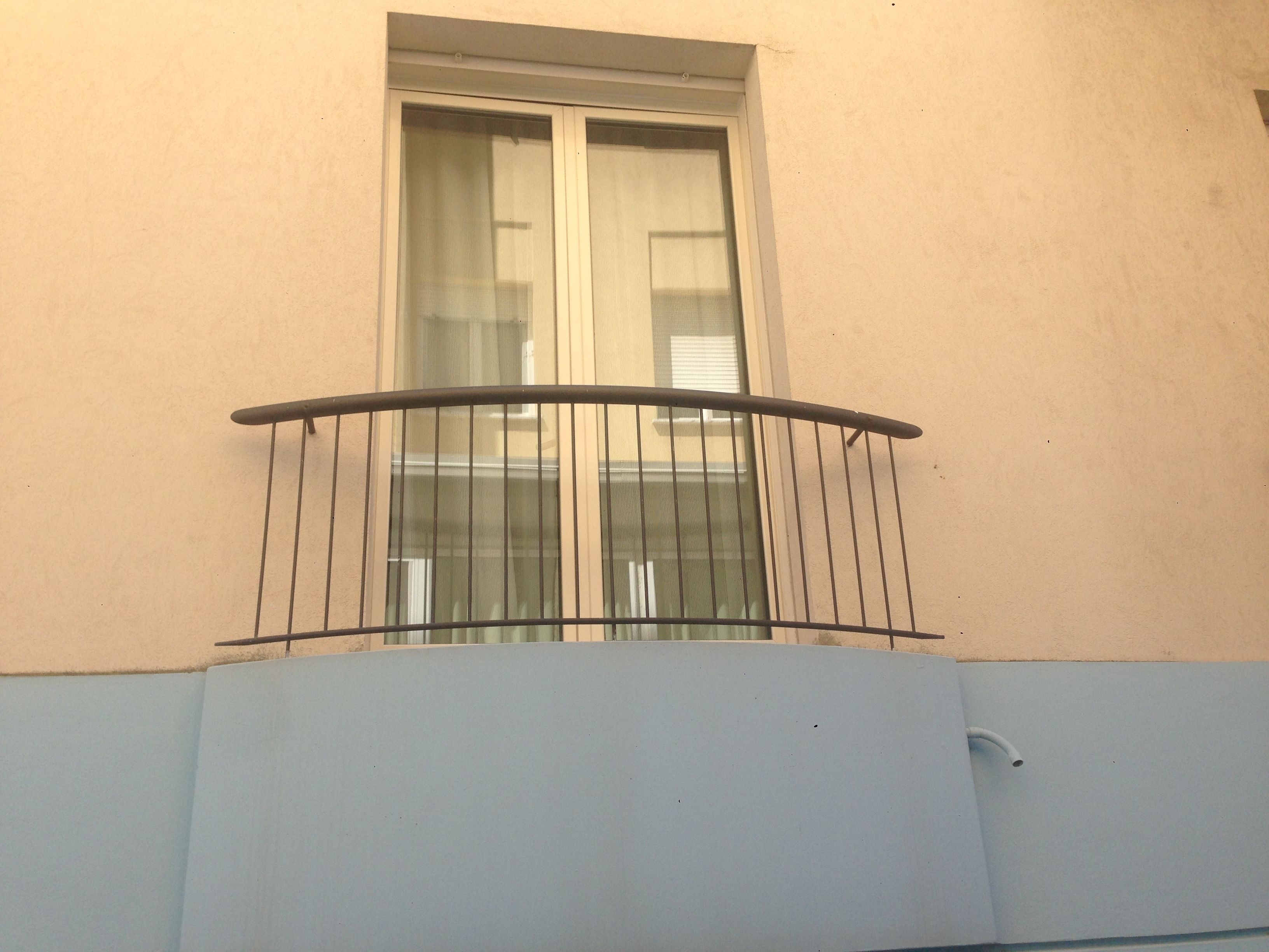 Un balcón con barandilla de metal y una ventana con persianas.