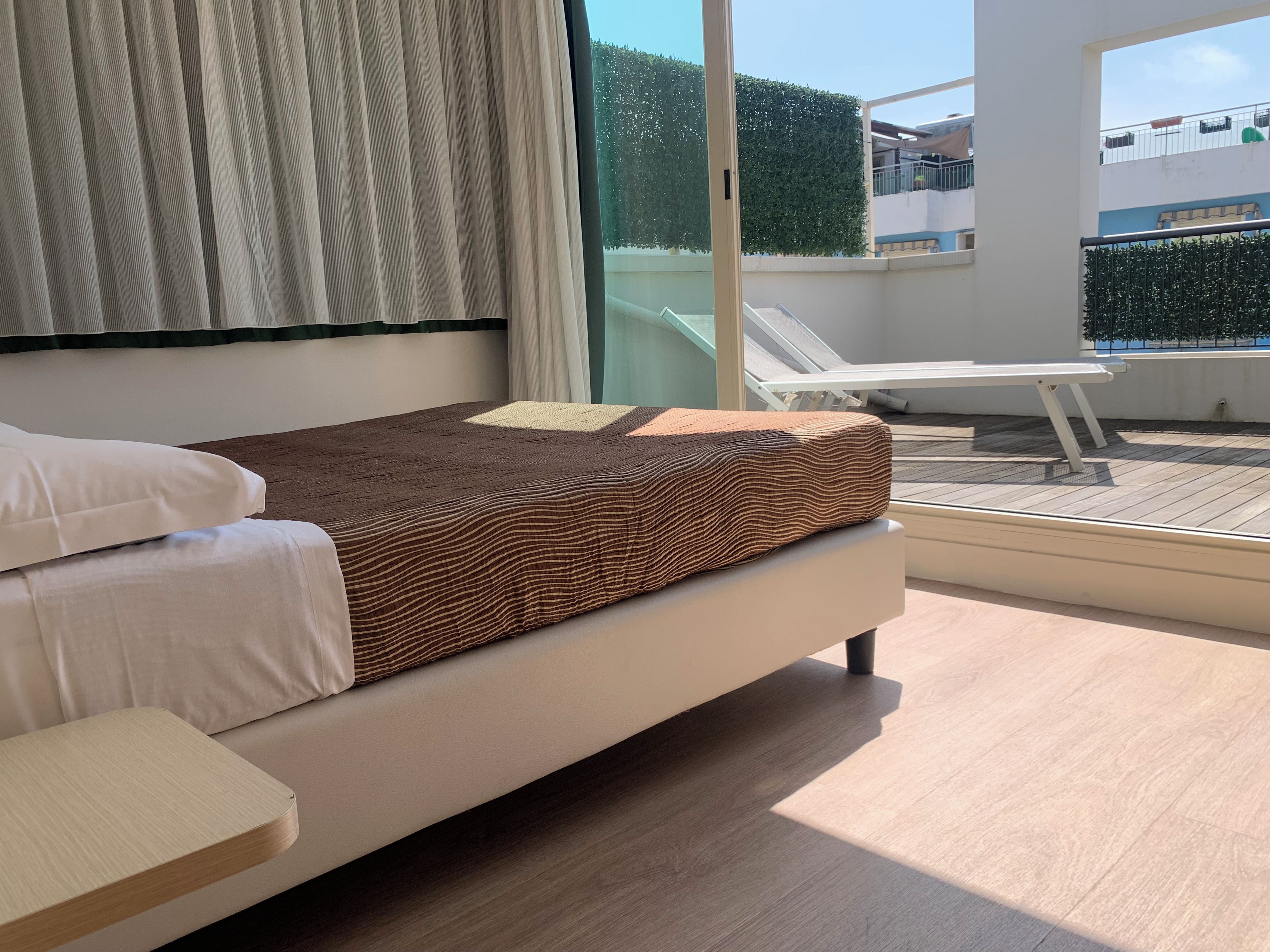 A bedroom with a bed, a bedside table, and a view of a balcony with a chair.