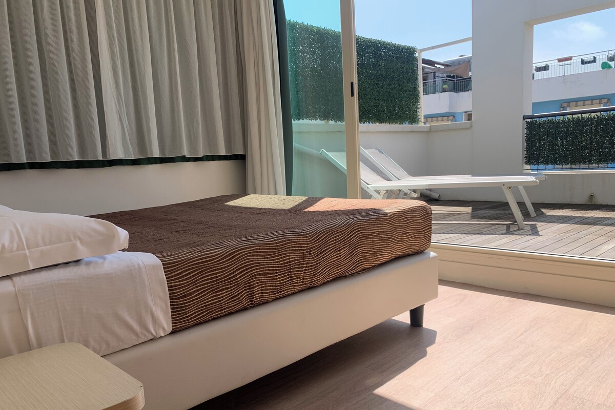A modern bedroom with a bed, a bedside table, and a view of the balcony.