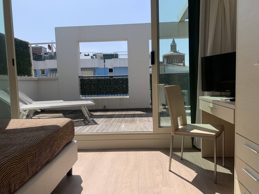 Un balcon avec un canapé blanc, une chaise et un téléviseur posé sur un meuble.