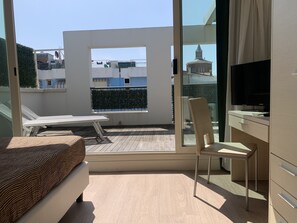 Un balcón con un sofá blanco, una silla y un televisor sobre un mueble.