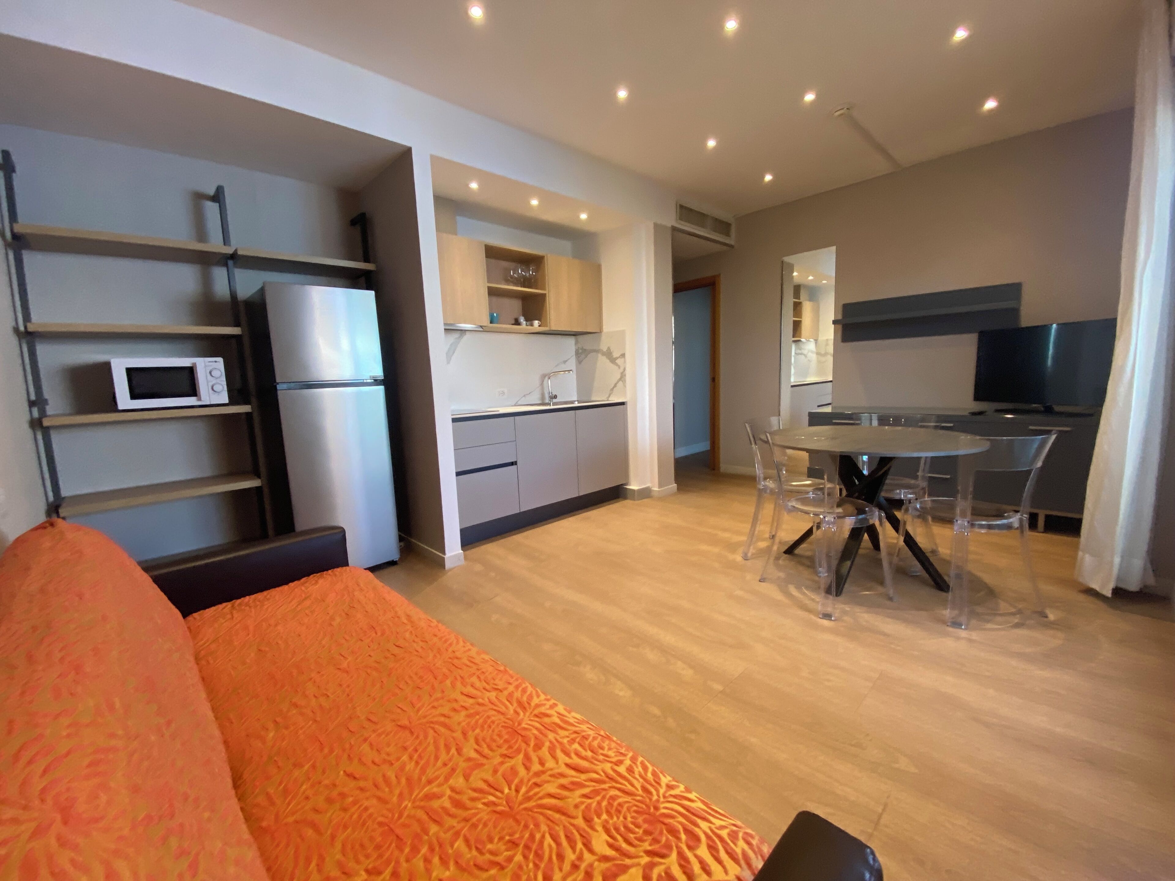 Un appartement moderne comprenant un canapé, une table à manger avec des chaises, un coin cuisine et un téléviseur.