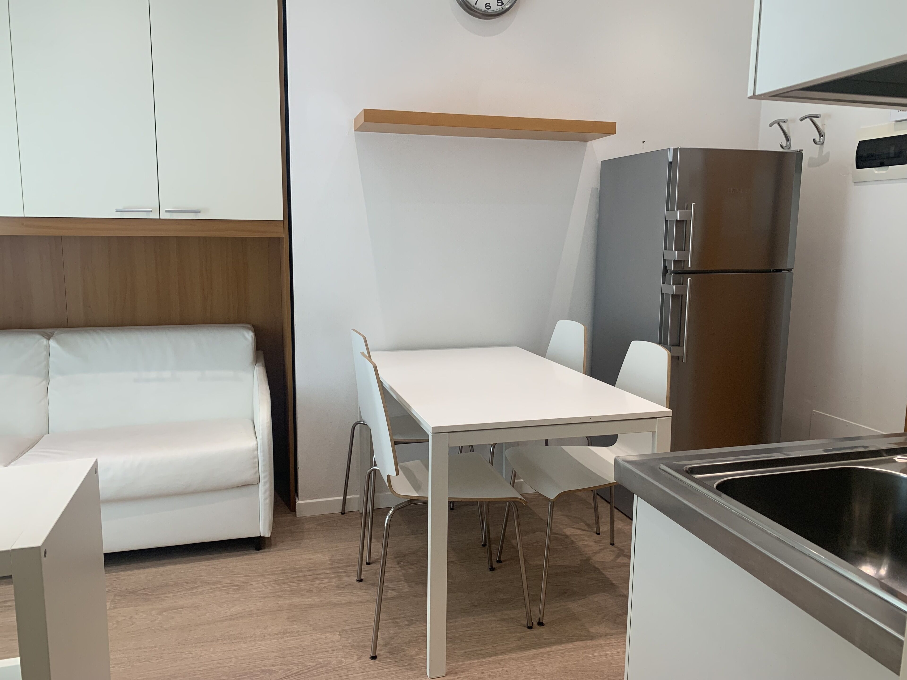 Una cocina moderna con armarios blancos, un refrigerador de acero inoxidable, una mesa de comedor blanca con sillas y un banco de madera.
