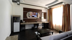 Una habitación de hotel moderna con kitchenette, televisión de pantalla plana, sofá y zona de comedor.