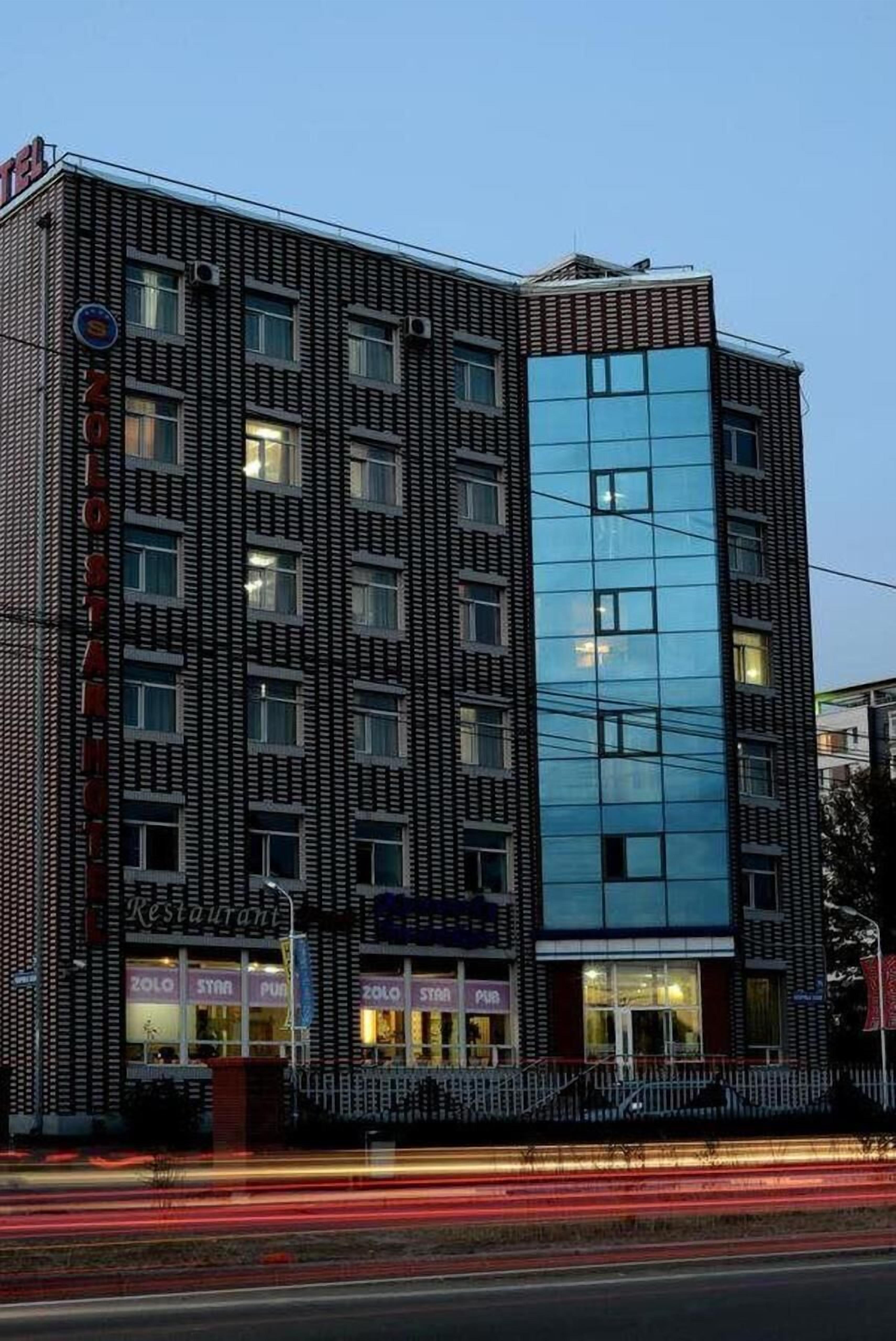 Un hotel moderno con fachada de vidrio, varios pisos y un restaurante visible llamado 'Zolo' a nivel de calle.