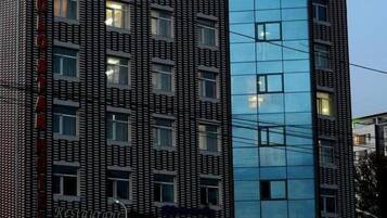 Un hotel moderno con fachada de vidrio, varios pisos y un restaurante visible llamado 'Zolo' a nivel de calle.